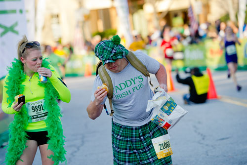 Jennifer Mann (left) and Eric Penney eat McDonalds and drink beer as they cross the finish line during the 2013 Publix Georgia Marathon/Half Marathon in Atlanta on Sunday, March 17, 2013. 