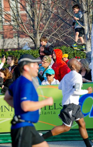 George Jardina (right) stands perched in a tree as he watches runners cross the finish line during the 2013 Publix Georgia Marathon/Half Marathon in Atlanta on Sunday, March 17, 2013.