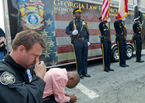 Atlanta Police Officer Patrick Magrum (left) wipes tears from his eyes as he holds William Smiley, the son of fallen Atlata Police Officer Shawn Smiley, on his knee during the unveiling of three officers' names on the Georgia Law Enforcement Memorial Wall outside of the Public Safety Headquarters in Atlanta on Thursday, April 11, 2013.