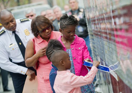 William Smiley (front), his sister Elizabeth, other sister Victoria and mother Terra pull away the tape covering their father Shawn's name with Atlanta Chief of Police George Turner (left) during the unveiling of three officers' names on the Georgia Law Enforcement Memorial Wall outside of the Public Safety Headquarters in Atlanta on Thursday, April 11, 2013. 