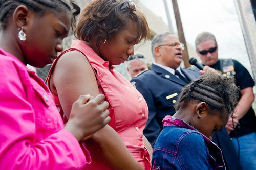 Victoria Smiley (left), her mother Terra and her sister Elizabeth bow their heads in prayer as Atlanta Police Chaplain Reginald Wilborn speaks during the unveiling of three officers' names on the Georgia Law Enforcement Memorial Wall outside of the Public Safety Headquarters in Atlanta on Thursday, April 11, 2013. 