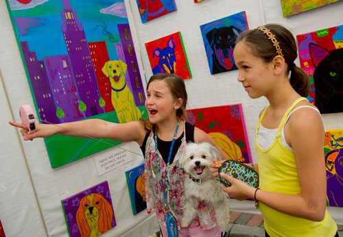 Amber Rae Proffitt (left) points out a painting that looks like her dog Lilly to her friend Halle Maya as they look at the artwork for sale in Angela Bond's booth during the Alpharetta Arts Streetfest on Saturday, April 13, 2013.
