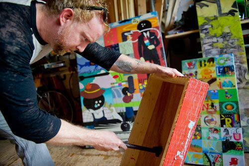 Smoke rises from the back of a frame as  Alex Wright brands the Urban Attic symbol to a mixed media piece that he and his partner Jennie Juechter created at their home in East Point on Tuesday, April 30, 2013. 