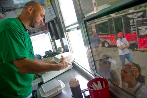 Troy Anglin (left) hands over an order to Meghan Benson and Jennifer Sperry from inside the One Love Jerk Grill truck at the Atlanta Food Truck Park & Market off of Howell Mill Road on Saturday, May 11, 2013. 