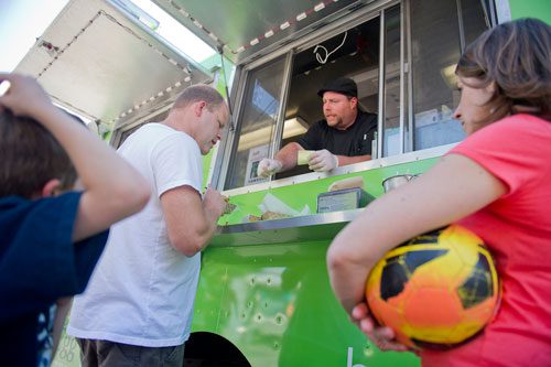 Bill Wooldridge (center) hands Matt Duncan (left) his order while Kasey Bradford (right) and her son Mason wait to pick up food from the Happy Belly food truck at Taylor-Brawner Park in Smyrna on Tuesday, May 14, 2013. 