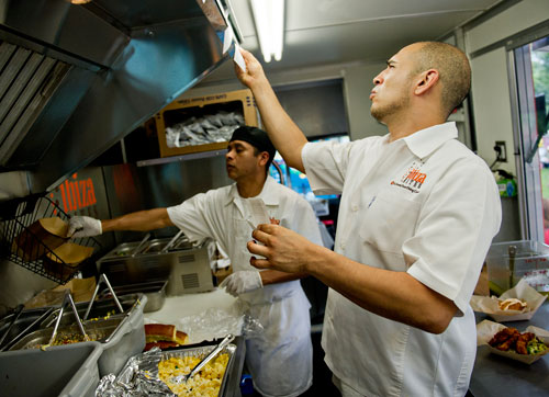 Miguel Morales (right) checks tickets as Sergio Vargas prepares food inside the Ibiza Bites truck during the Atlanta Street Food Festival at Piedmont Park on Saturday, July 13, 2013. 