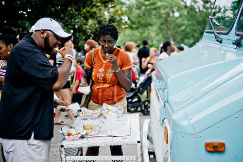 Brian Walker (left) and his wife Temitope use the front of a food truck to eat lunch during the Atlanta Street Food Festival at Piedmont Park on Saturday, July 13, 2013. 