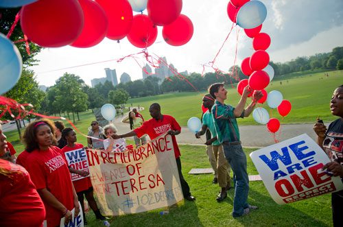 Robert Feria (right) loosens ballons as Thomas Otoo passes one to Aimee Twagirumukiza as participants prepare for a moment of silence during the We Are Here Rally for Respect in Rememberance of Teresa Weaver Pickard at Piedmont Park in Atlanta on Wednesday, June 26, 2013. 