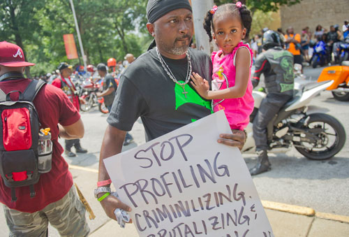 Jermaine McBryde carries his daughter Janaya and a sgn during the Trayvon Martin Rally at the Georgia State Capitol in Atlanta on Sunday, July 28, 2013. 