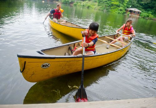 Celina Speir (left) and Dakota Pasley manuever their canoe as they near the dock while Aubrey Bowen shouts directions through a megaphone during Camp Kingfisher at the Chattahoochee Nature Center in Roswell on Wednesday, June 5, 2013. 