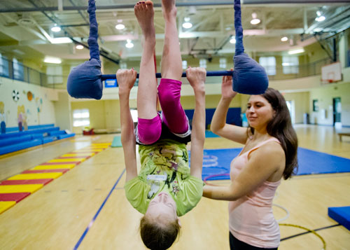 Annika Callaham (center) hangs from a trapeze as junior counselor Allie Goodman helps steady her during Circus Summer Camp at Davis Academy in Dunwoody on Wednesday, July 10, 2013. 