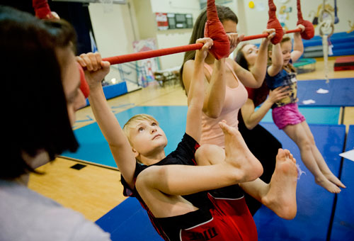 Spencer Burdett (left) pulls himself onto a triple trapeze next to junior counselor Allie Goodman as instructor Liz Ramsay helps steady Flynn Peljovich during Circus Summer Camp at Davis Academy in Dunwoody on Wednesday, July 10, 2013. 