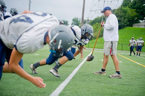 Norcross defensive tackle coach Corey Richardson (right) runs Traivon Mackey (center) and other players through warmups during practice on Wednesday, August 21, 2013. 