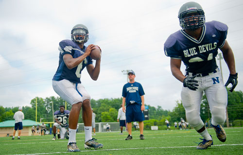 Norcross' A.J. Bush (left) is hiked the ball as he runs a play with James Keeling during practice under the watchful eye of quarterback coach Steve Sims on Wednesday, August 21, 2013.