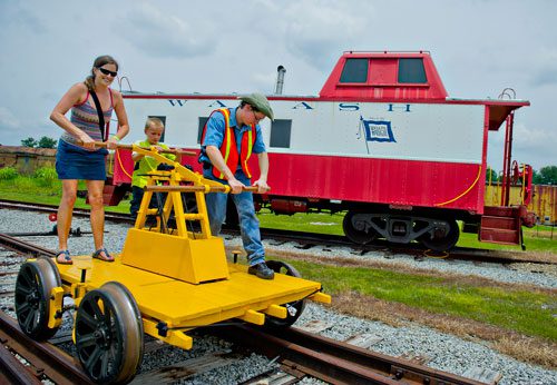Aleta Mills-Stubin (left), her son Henry Stubin and Alex Grey work to move an 1890s era Sheffield hand car along the tracks during Trains, Trucks and Tractors at the Southeastern Railway Museum in Duluth on Saturday, August 3, 2013.