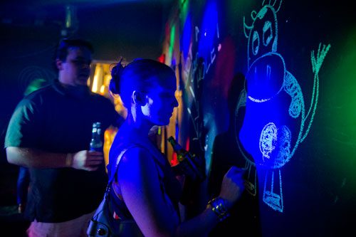 Keri Toggerson (center) writes graffiti on the wall as Andrew Spratt watches during the Bringing Down the House Party at Dad's Garage in Atlanta on Saturday, August 3, 2013. 