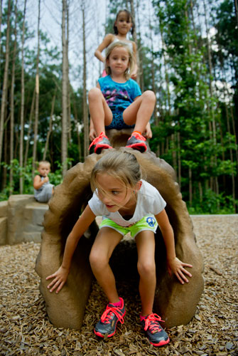 Riley Burke crawls through a log as her sister Kensley and Sophie Haney sit on top at the playground at Caney Creek Preserve in Cumming on Friday, August 9, 2013.