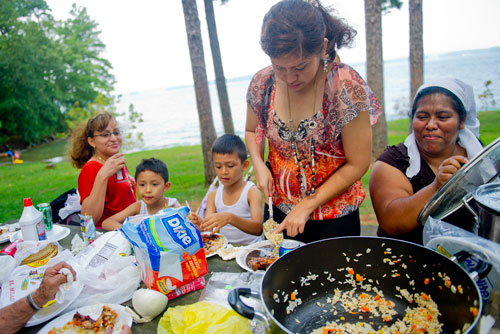 Teresa Herrera (right) holds a lid as Yuseli Ramirez takes a spoonful of food as they eat with Julio DeLeon, his brother Josue and Brenda Ramirez at Van Pugh Park on the shore of Lake Lanier in Flowery Branch on Sunday, September 1, 2013. 