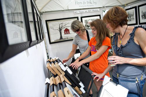 Beth Martin (left) and Cara Granelli and her mother Amy look at the sketches on display in Marjorie Bowers' booth during the Atlanta Arts Festival at Piedmont Park on Sunday, September 15, 2013. 