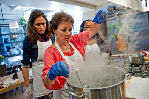 Martha McMillin (center) places a jar of pear preserves into a pot of boiling water as Kristin Stockton (left) and Morgan Dooley (right) watch as she teaches a canning class at The Preserving Place in Atlanta on Saturday, September 14, 2013. 
