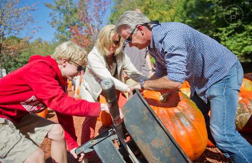 Brendan Spillane (left), Beth Spillane and Skeet Pillane lift thier pumpkin into a wheelbarrow at Burt's Pumpkin Farm in Dawsonville on Sunday, October 13, 2013.