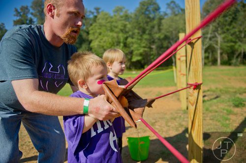 Jason Tarpley (left) helps his son Caiden aim the pumpkin slingshot as his other son Ary watches at the Still Family Farm in Powder Springs on Saturday, October 5, 2013. 