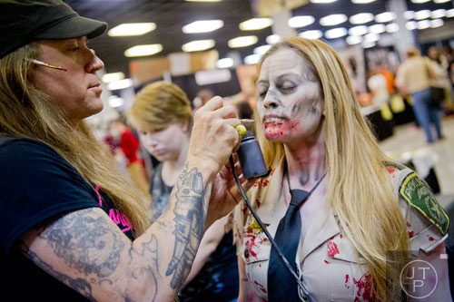 Shane Morton (left) sprays paint on Jenny Loaiza's face as he turns her into a zombie during Walker Stalker Con at the Atlanta Convention Center at AmericasMart on Saturday, November 2, 2013. 