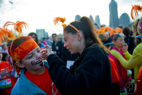 Kristen Courtemanche (left) gets help with her fake moustache from Emily Dawley before the start of the 2013 Girls on the Run 5k at Atlantic Station in Atlanta on Sunday, November 10, 2013. 