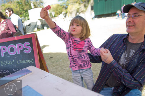 Ruby Blair (center) holds out her ticket for a free popsicle as he father Lance kneels beside her during the 3rd Annual King of Pops Field Day at Masquerade Music Park in Atlanta on Sunday, November 10, 2013.