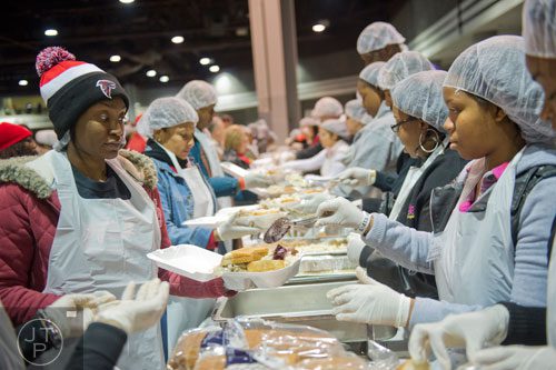 Naquonna Glenn (left) carries trays of food down a line of volunteers as Katera Samuel spoons cranberry sauce onto them during the Hosea Feed the Hungry and Homeless annual Thanksgiving meal at the Georgia World Congress Center in Atlanta on Thursday, November 28, 2013.