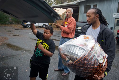 Eric Willie (right) and James Hampton carry Thanksgiving supplies to TJ Flagg's family's car as he opens the trunk at the Philip Rush Center in the Edgewood neighborhood of Atlanta on Sunday, November 17, 2013.