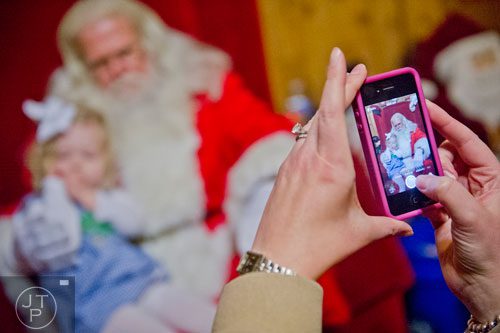 Allie Hill (right) uses her phone to take a photo of her daughter Olivia as she visits with Santa at Ronald and Betty Page's home in Canton on Thursday, December 12, 2013. 