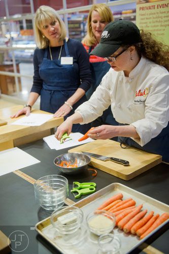 Chef Samantha Enzmann (right) explains how she wants carrots peeled and sliced for a recipe as Laurel Mackenzie and Susan Hall watch during a cooking class at the Salud Cooking School at Harry's Farmers Market in Roswell on Thursday, January 23, 2014.