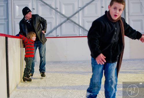 Jadon Coover (left) hangs on the wall of the rink with his father Jeff as they watch people ice skate  at Centennial Olympic Park in downtown Atlanta on Sunday, December 8, 2013.   
