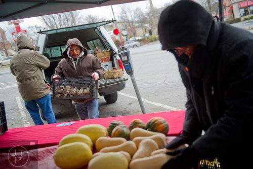 Antonio Garcia (center) walks towards the Mountain Earth Farms booth with a crate of vegetables as Tina Mathis (right) places squash on the table at the Decatur Farmers Market on Saturday, January 4, 2014. 