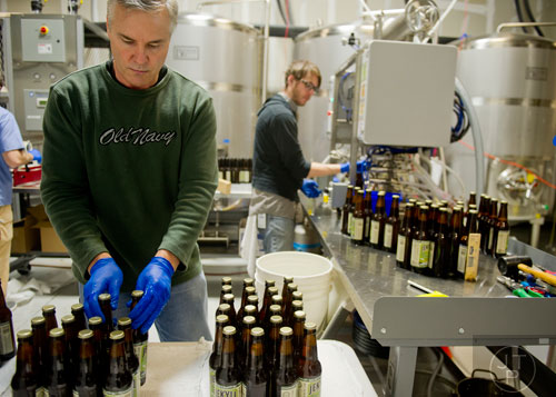 Gregg Dickson (left) moves capped bottles to the packaging area as Richard Oakes fills more at Jekyll Brewing in Alpharetta on Tuesday, February 18, 2014. 