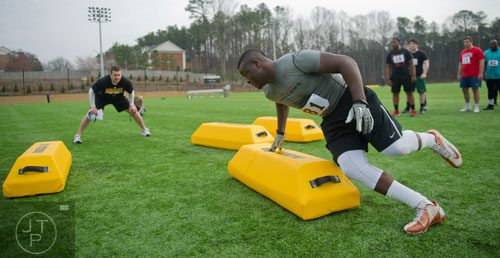 Isidore Sam (right) cuts hard around a bag as coach Shane Bowen watches in a linebacker drill during the first tryouts for the new Kennesaw State University football team at The Perch on campus on Saturday, March 22, 2014. 