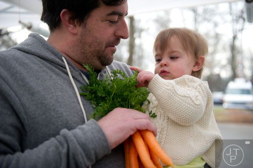 Alex Sithens (left) lets his daughter Abigail feel a bunch of carrots at the Woodland Gardens booth during the Freedom Farmers Market at the Carter Center in Atlanta on Saturday, March 1, 2014. 