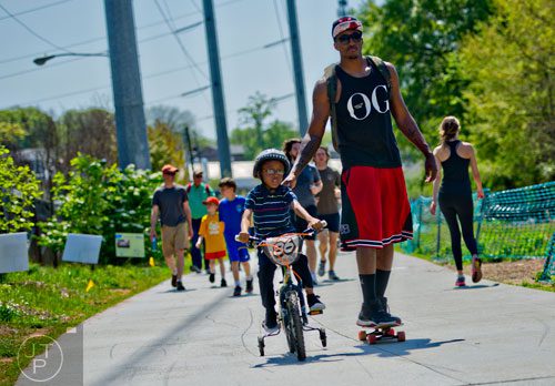 Lecrae Moore (right) rides his skateboard as his son David rides his bike down the path along the Atlanta Beltline Trail on Saturday, April 12, 2014.  