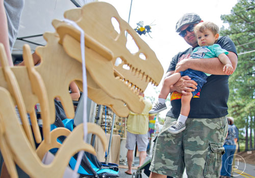 Christian Novacek (center) holds his son Nixon as they check out a wooden dinosaur at Paul Fussell's booth during the Sandy Springs Artsapalooza on Sunday, April 13, 2014. 