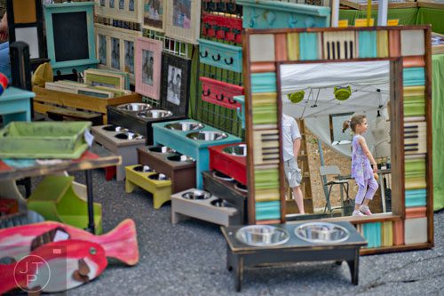 Tayla Berzack (right) is reflected in a mirror as she passes by Suzanne and Don Puckett's booth during the Sandy Springs Artsapalooza on Sunday, April 13, 2014. 