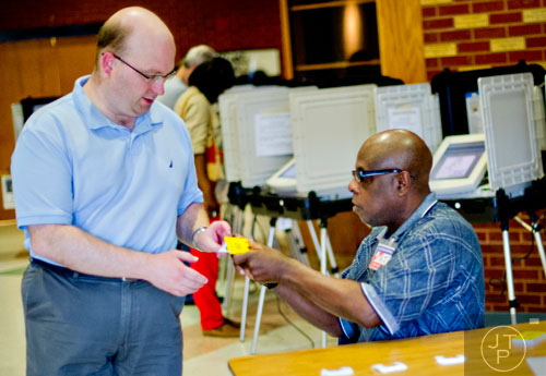 Chris Miller (left) hands his voting card to poll worker AJ McAdory after he finishes casting his ballot at the North Fulton polling location at Centennial High School in Roswell on Tuesday, May 20, 2014. 