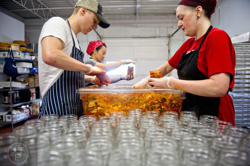 Ben Wills (left) and Lollie Nabors (right) fill jars with freshly prepared kimchi as Hannah Chung screws lids on already filled jars at the Simply Seoul Kitchen in Decatur on Thursday, May 15, 2014.   