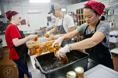 Hannah Chung (right) rinses jars of kimchi as Ben Wills and Lollie Nabors (left) fill more jars at the Simply Seoul Kitchen in Decatur on Thursday, May 15, 2014.   