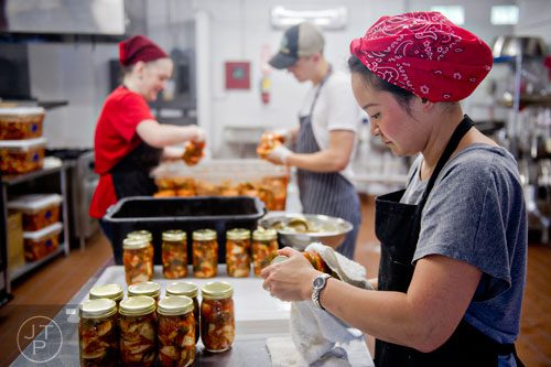 Hannah Chung (right) dries jars of kimchi as Ben Wills and Lollie Nabors (left) fill more jars at the Simply Seoul Kitchen in Decatur on Thursday, May 15, 2014. 