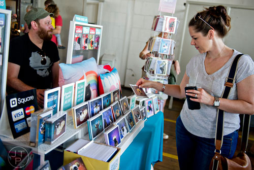 Brenna Maschinot-Dorsey (right) picks up a card as Jay Anderson helps man his wife's booth during the Indie Craft Experience at Ambient Plus Studio in Atlanta on Saturday, June 28, 2014. 