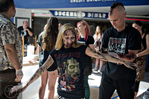 Kasey Kyner (left) spreads her arms as Jason Feeman applies makeup to make her look like a walker during The Walking Dead Escape event at Philips Arena in Atlanta on Saturday, May 31, 2014. 