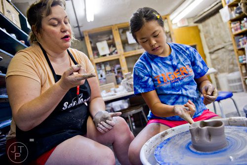 Instructor Laura Martin (left) helps Ainslee Coombs as she throws clay on a wheel during Summer Youth Art Weeks at the Abernathy Arts Center in Sandy Springs on Wednesday, June 4, 2014. 