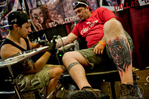 James Knight (right) sports a fresh tiger tattoo on his leg as Wil Hilderbrand works on a new tattoo on his arm during the Atlanta Tattoo Expo at the Wyndham Atlanta Galleria hotel on Saturday, June 7, 2014. 