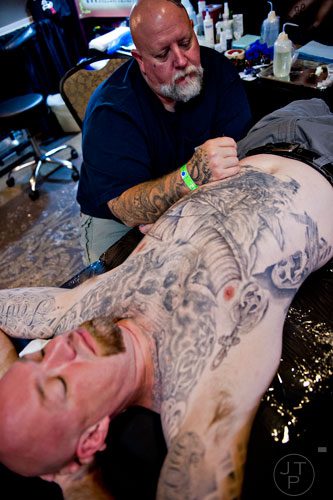 Brent Roman (top) works on a tattoo design for Kyle Downie's stomach during the Atlanta Tattoo Expo at the Wyndham Atlanta Galleria hotel on Saturday, June 7, 2014. 